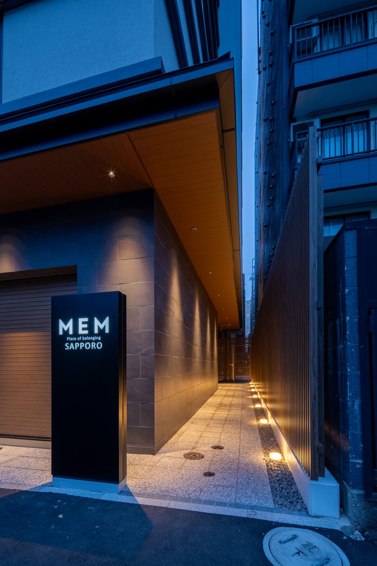 夜のアプローチ。灯りのともる MEM SAPPORO のサインと足元灯